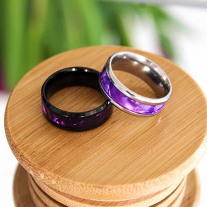 May include: Two rings with purple inlay. One ring is black and the other is silver.
