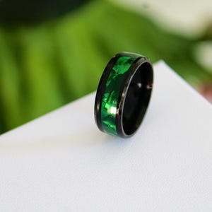 May include: A black ring with a green inlay. The ring is made of metal and has a polished finish.