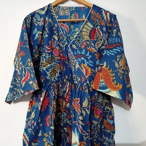 May include: A blue cotton tunic with a floral print in shades of red, orange, yellow, and green. The tunic has a V-neckline and a wrap-style closure.