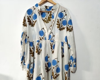 Può includere: Un abito bianco a maniche lunghe con stampa floreale blu e marrone. L'abito ha una scollatura a V e una chiusura con bottoni sul davanti.
