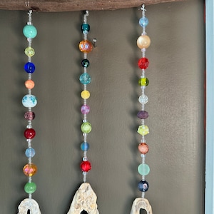 May include: Three strands of colorful beads hang from a wooden beam. Each strand features a different color scheme, including turquoise, blue, orange, yellow, green, red, purple, and brown beads.