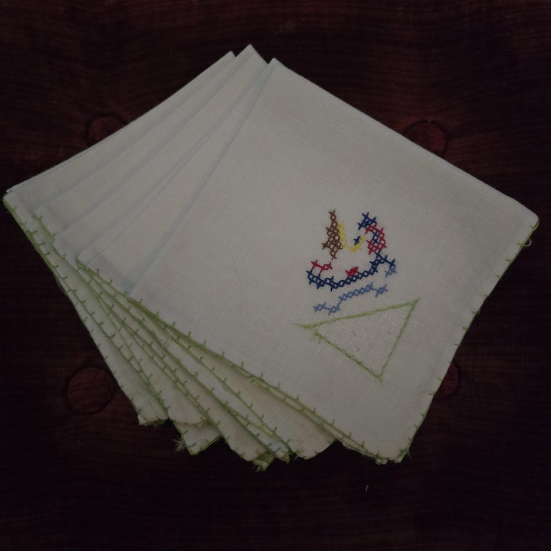 Puede incluir: Juego de seis servilletas de lino blanco con bordes bordados en verde. Cada servilleta presenta un dise&ntilde;o de velero bordado en punto de cruz de colores.