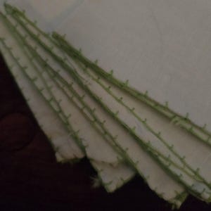 Puede incluir: Una pila de servilletas de tela blanca con un borde cosido verde.