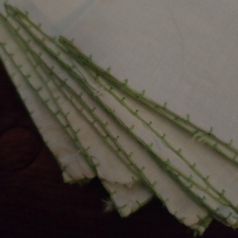 Puede incluir: Una pila de servilletas de tela blanca con un borde cosido verde.