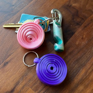May include: Two keychains with colorful, layered, circular designs. One keychain is pink and the other is purple.