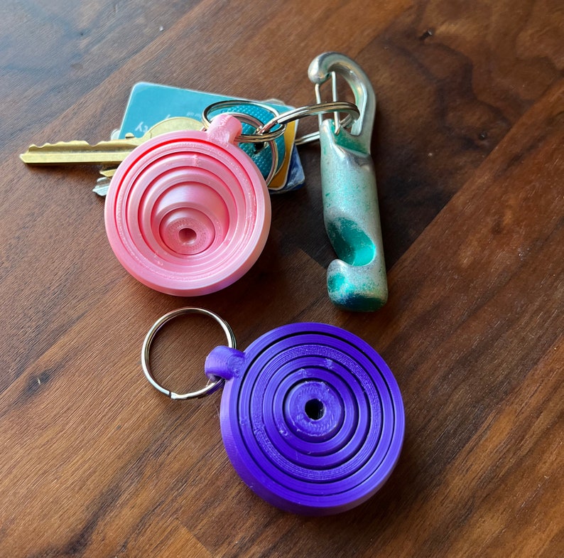 May include: Two keychains with colorful, layered, circular designs. One keychain is pink and the other is purple.