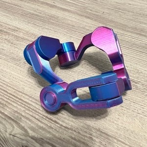 May include: A 3D printed plastic object with a blue and purple iridescent finish. The object has a complex shape with multiple curves and angles.