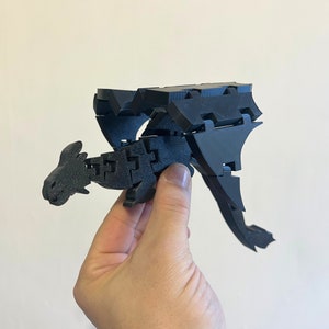 May include: A black 3D printed dragon model with articulated wings and a detailed head. The dragon is posed in flight with its wings spread.
