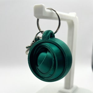 May include: A green 3D printed keychain with a swirling design. The keychain is attached to a silver key ring.