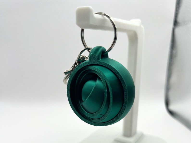 May include: A green 3D printed keychain with a swirling design. The keychain is attached to a silver key ring.