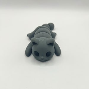 Peut inclure: Une figurine de chat grise imprimée en 3D avec une queue enroulée. Le chat a des yeux noirs et un petit nez.