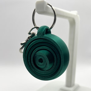May include: A dark green spiral keychain with a silver key ring. The spiral is made of multiple layers of plastic and has a smooth, rounded surface.
