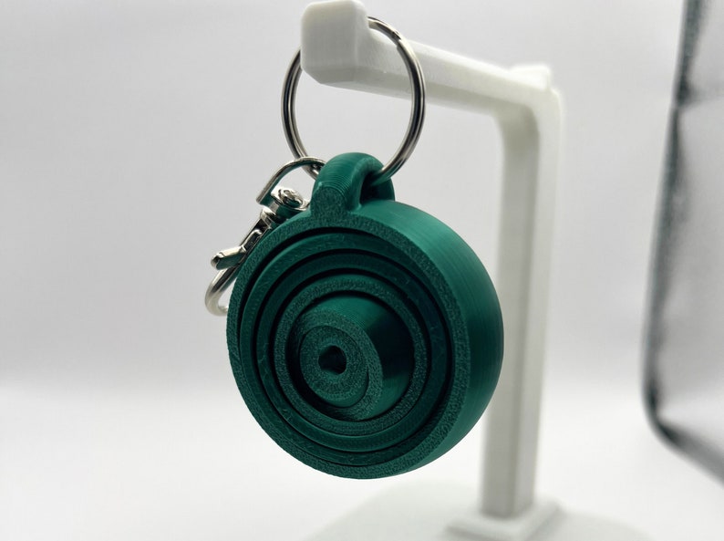 May include: A dark green spiral keychain with a silver key ring. The spiral is made of multiple layers of plastic and has a smooth, rounded surface.