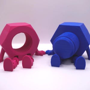 May include: Two whimsical, anthropomorphic nuts. One is a vibrant pink nut with a large central hole, and the other is a deep blue bolt. Both have small arms and legs, giving them a playful appearance. They are set against a plain white background.
