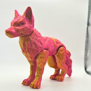 May include: A pink and gold articulated fox figurine. The fox is standing on all four legs with its tail curled behind it. The figurine is made of plastic and has a textured surface.