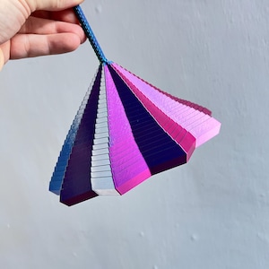 May include: A fan-shaped color swatch with a blue handle and a spectrum of colors from blue to pink. The color palette includes shades of blue, silver, purple, and pink. The object is held by a hand.
