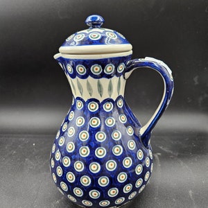 May include: A blue and white ceramic pitcher with a lid. The pitcher has a round body with a pattern of blue and white circles. The lid has a similar pattern.