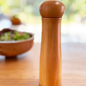 May include: A wooden salt or pepper grinder with a rounded top and a natural wood finish.