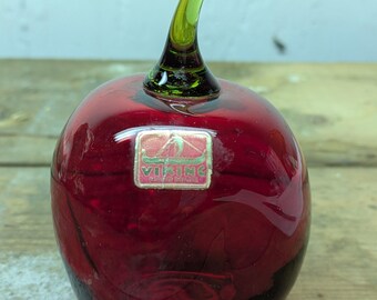 May include: A red glass apple with a green glass stem. The apple has a label that says "Viking Glass, Made in Finland."