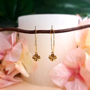 Peut inclure: Une paire de boucles d'oreilles créoles en or avec un petit charme trèfle à quatre feuilles suspendu à chaque créole.