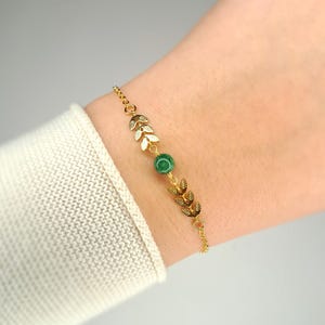 Könnte beinhalten: Ein goldenes Kettenarmband mit einem grünen Edelstein und goldenen Blatt-Anhängern.
