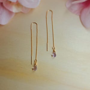 Könnte beinhalten: Ein Paar goldene Kettenohrringe mit zarten rosa Edelstein-Tropfen.