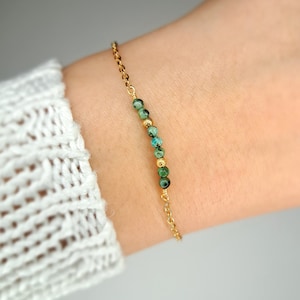 Könnte beinhalten: Ein goldenes Kettenarmband mit grünen Edelsteinperlen.