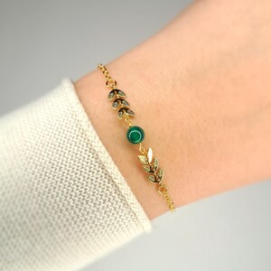 Könnte beinhalten: Ein goldenes Kettenarmband mit einem grünen Edelstein und goldenen Blattakzenten.