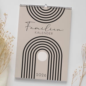 Könnte beinhalten: Ein beiger Wandkalender mit schwarzen geometrischen Bogenmustern und dem Text "Familien KALENDER 2026". Der Kalender ist oben spiralgebunden und hat eine minimalistische, moderne Ästhetik.