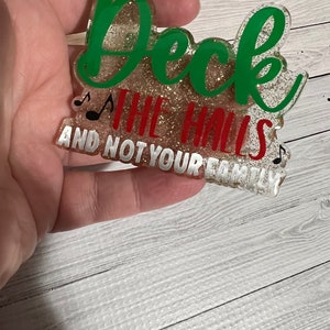 May include: A glittery gold and green Christmas ornament with the text "Deck the halls and not your family".