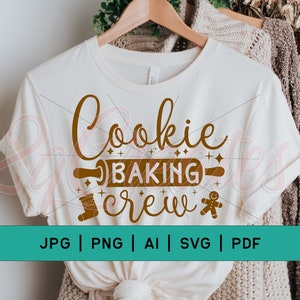 Puede incluir: Una camiseta blanca con el texto "Cookie Baking Crew" en letras marrones. El texto está decorado con un rodillo, un hombre de jengibre y una media.