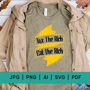 Peut inclure: Un t-shirt vert avec un graphique jaune qui dit "Tax The Rich Eat The Rich". Le t-shirt est posé sur une surface en bois avec une veste marron et un jean bleu.