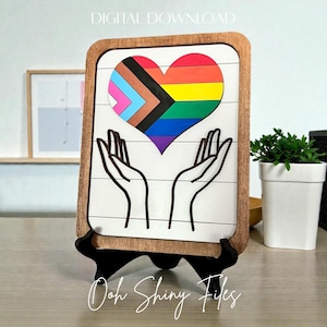May include: A wooden sign featuring a heart in the colors of the Pride flag, with hands reaching up to support it. The sign has a white background with horizontal lines and a brown wooden frame. The words "DIGITAL DOWNLOAD" are at the top.