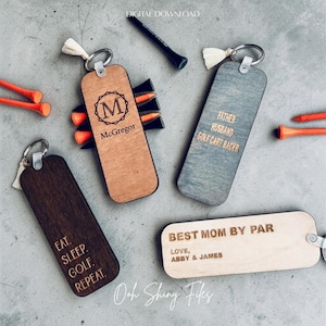 May include: A collection of wooden keyrings with golf-related inscriptions. Keyrings include phrases like "Eat. Sleep. Golf. Repeat" and "Best Mom by Par". Other keyrings have the text "McGregor" and "Father, Husband, Golf Cart Racer."