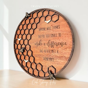 May include: A round wooden sign with a honeycomb design and the quote, "Anyone who thinks they're too small to make a difference has never met a honeybee." The sign features small bee and honeycomb accents.