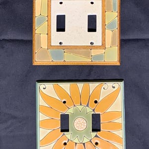 Peut inclure: Deux plaques décoratives pour interrupteurs. La plaque supérieure présente un motif en mosaïque aux couleurs terreuses. La plaque inférieure présente un motif de tournesol avec des pétales orange et un centre vert. Les deux ont deux ouvertures pour interrupteurs.
