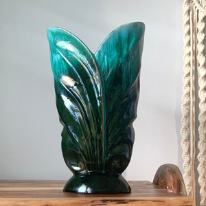 May include: A green and blue ceramic vase with a leaf design. The vase is tall and slender, with a wide opening at the top. It has a glossy finish and is made in the style of a vintage piece.