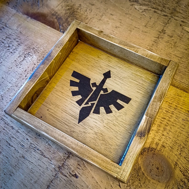 May include: A wooden dice tray with a black and white eagle and sword design. The tray is made of natural wood and has a clear acrylic insert.