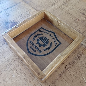 May include: A wooden tray with a black and white logo that says "House of Steel Wargaming Teesside". The logo features a gear with a hard hat on top of it.