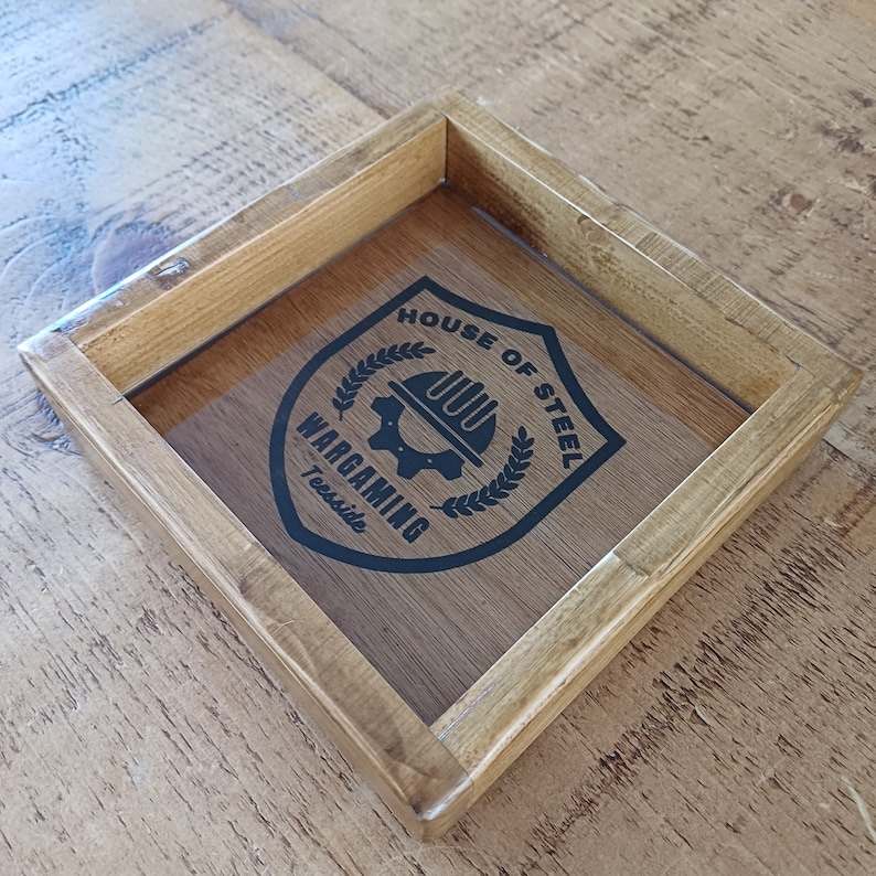 May include: A wooden tray with a black and white logo that says "House of Steel Wargaming Teesside". The logo features a gear with a hard hat on top of it.