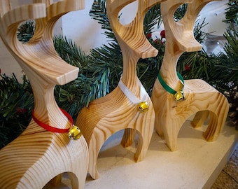 May include: Three wooden reindeer ornaments with gold bells. The reindeer are painted in natural wood tones and have white, green, and red ribbon around their necks.