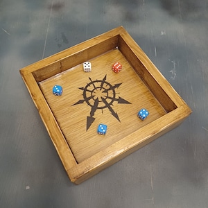 May include: A wooden dice tray with a black and white symbol in the center. There are five dice inside the tray, two blue, one red, and two white.