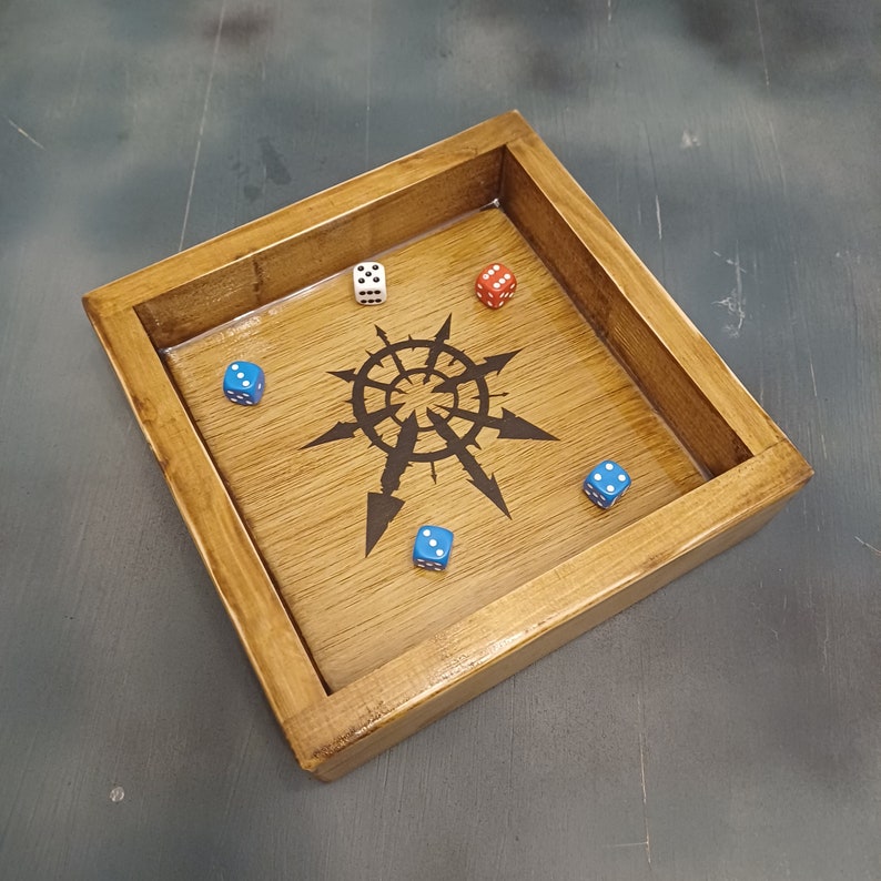 May include: A wooden dice tray with a black and white symbol in the center. There are five dice inside the tray, two blue, one red, and two white.