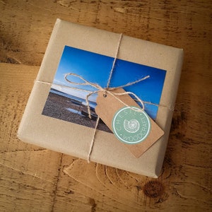 May include: A brown paper package tied with twine and a green and white gift tag that says "Chesil Woodcraft". The package has a photo of a beach scene with a blue sky and a boat.