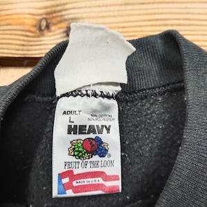 May include: A black Fruit of the Loom sweatshirt tag with white text. The tag reads "Adult L 50% Cotton 50% Polyester Heavy Fruit of the Loom Made in U.S.A."