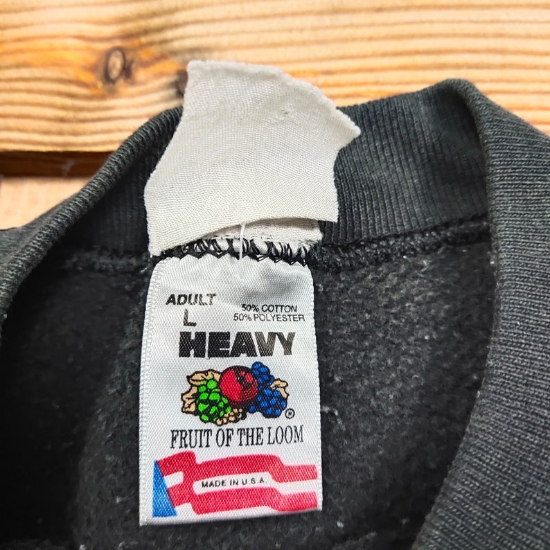 May include: A black Fruit of the Loom sweatshirt tag with white text. The tag reads "Adult L 50% Cotton 50% Polyester Heavy Fruit of the Loom Made in U.S.A."