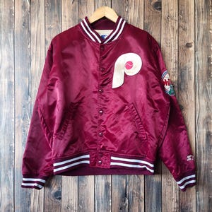 Peut inclure: Une veste de baseball en satin marron avec des bordures blanches et rouges autour du col, des poignets et de l'ourlet. La veste a un grand "P" brodé en or sur la poitrine gauche et un petit patch sur la manche droite. La veste est de style vintage.