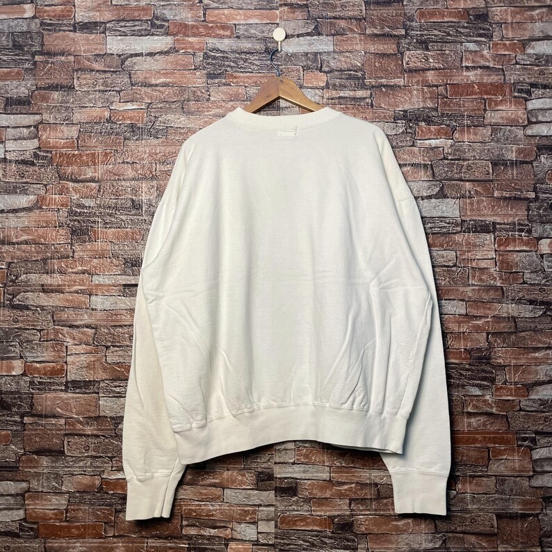 May include: A white crew neck sweatshirt with long sleeves and a relaxed fit.