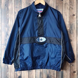 Puede incluir: Una chaqueta cortavientos azul marino con detalles en blanco y negro. La chaqueta tiene una cremallera de media cremallera y un gran logotipo de estrella en la parte delantera. El logotipo está rodeado de un óvalo azul y blanco con el texto "PRO LINE" encima.