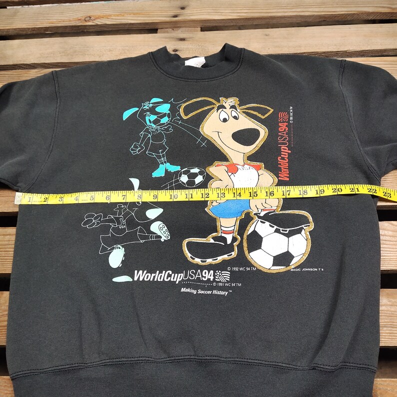 May include: Black sweatshirt with a graphic print of a cartoon dog and a soccer ball. The text "World Cup USA 94" and "Making Soccer History" is printed on the sweatshirt.